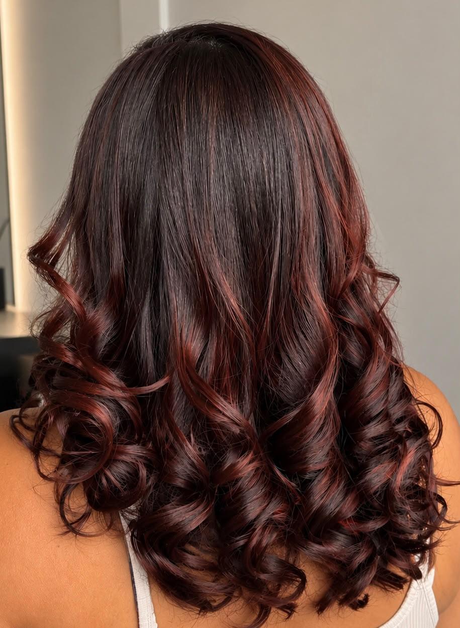 Cabelo castanho com reflexos vinho e cachos modelados nas pontas, visto de costas